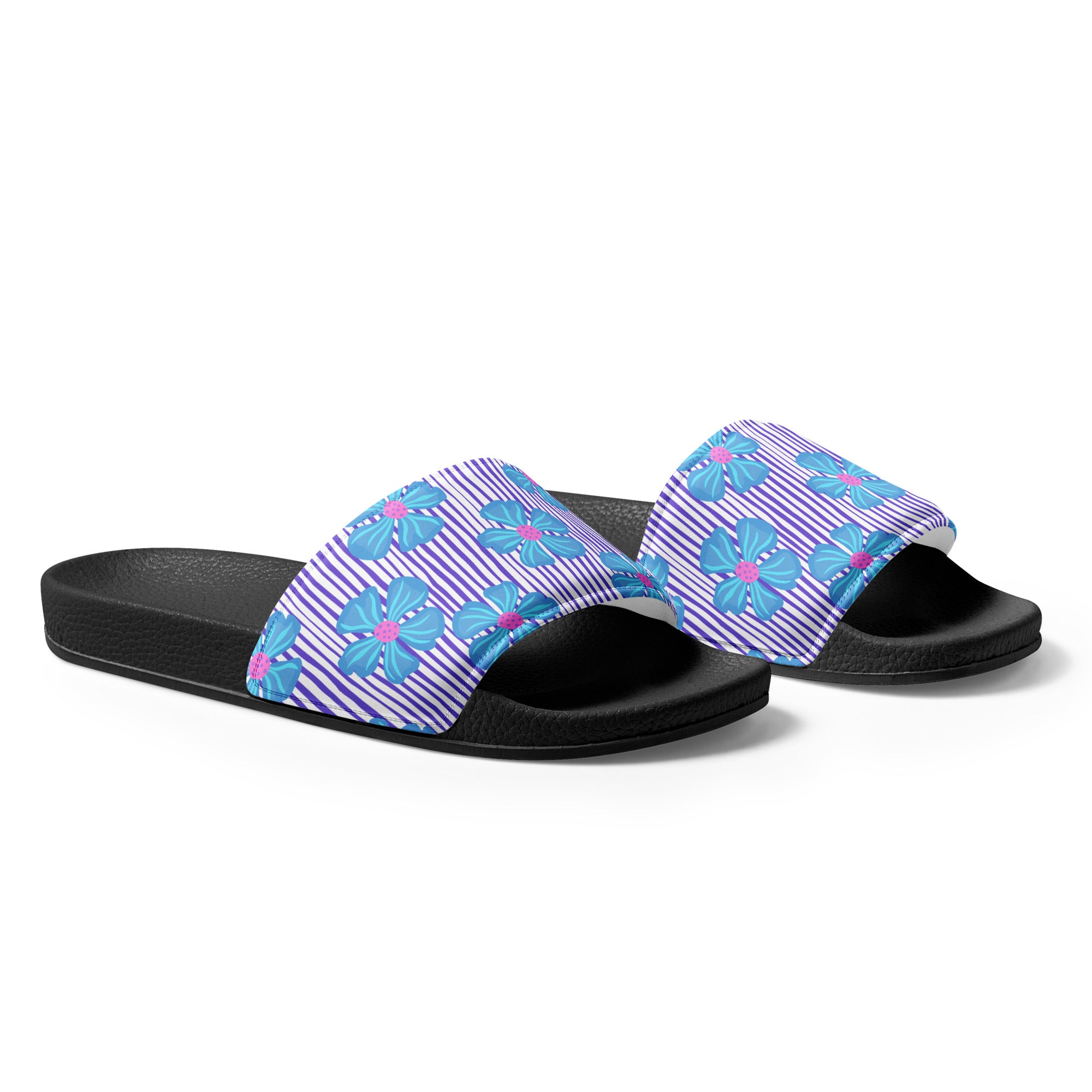 Ein Paar schwarze Damen-Badeschlappen mit einem breiten Riemen. Der Riemen ist mit einem Muster aus vertikalen lila und weißen Streifen versehen, die von großen, stilisierten blauen Blüten mit pinkfarbenen Zentren überlagert werden. Die Sohle ist schwarz und hat eine leicht texturierte Oberfläche.