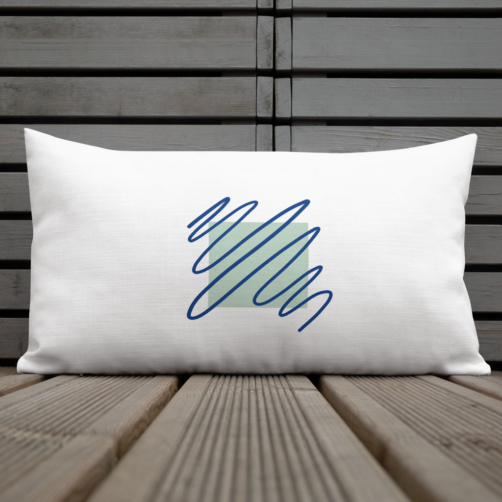 Ein weißes Kissen mit einem quadratischen, hellgrünen Muster im Zentrum. Darüber sind blaue, gekritzelte Linien zu sehen. Das Kissen liegt auf einem Stuhl, und links im Bild ist ein Teil eines kleinen Tisches mit einer weißen Tasse zu erkennen. Das Kissen ist in der Größe "20 x 12" erhältlich. Designed, by Just a Girl