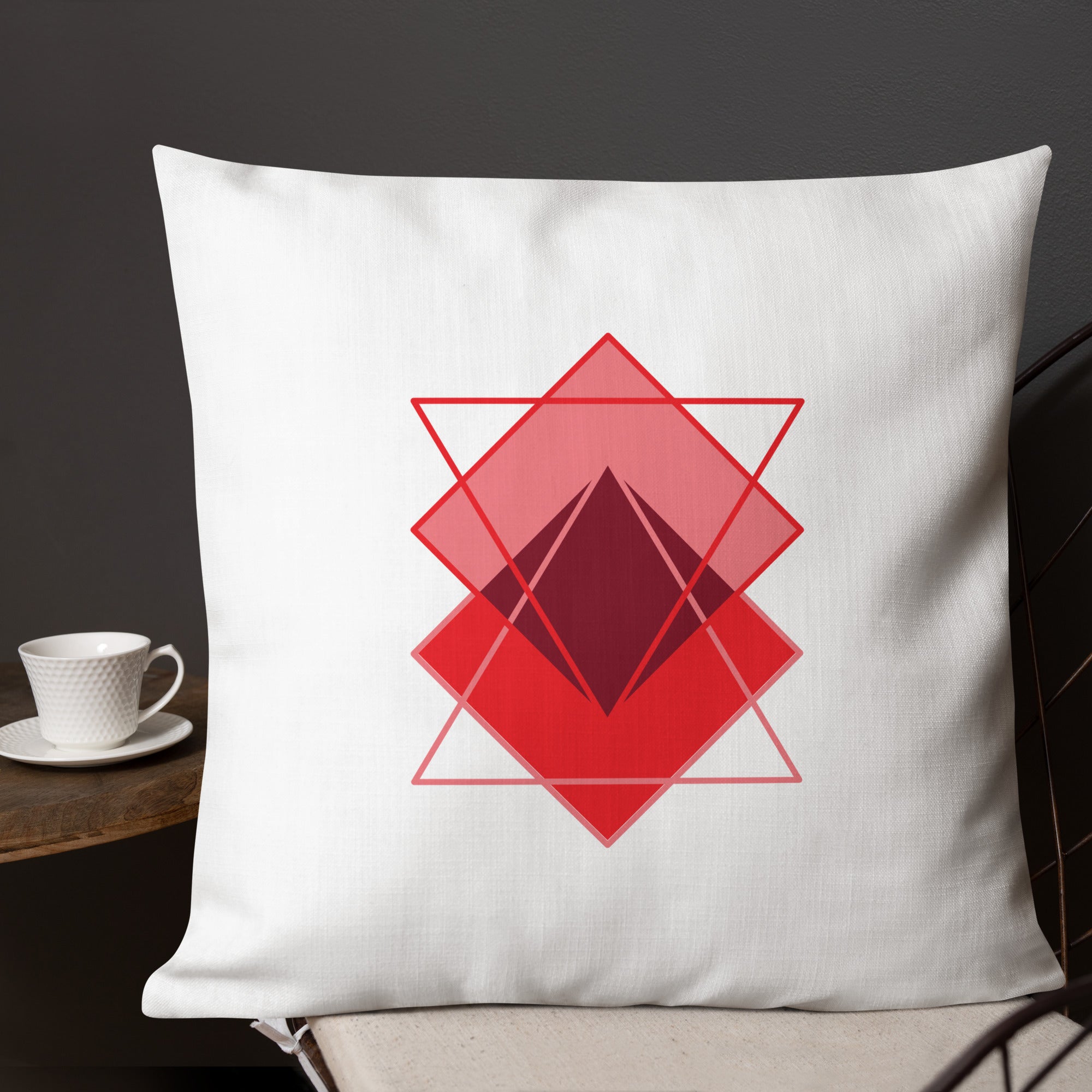 Ein Dekokissen der Grundton ist cremeweiß ist mit einem minimalistischen abstrakten Motiv aus überlappenden, roten und rosafarbenen geometrischen formen in der Größe 22"x22".